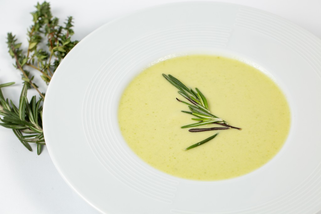 Shot of a soup plate with Zucchini Cream soup on a white table decorated with green plants