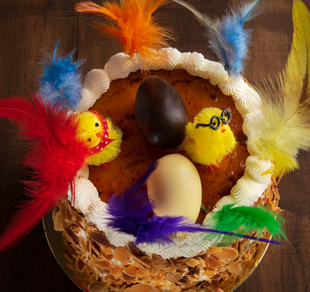 Closeup of a mona de pascua, a cake eaten in Spain on Easter Monday, ornamented with feathers and a teddy chick on on a rustic wooden surface.