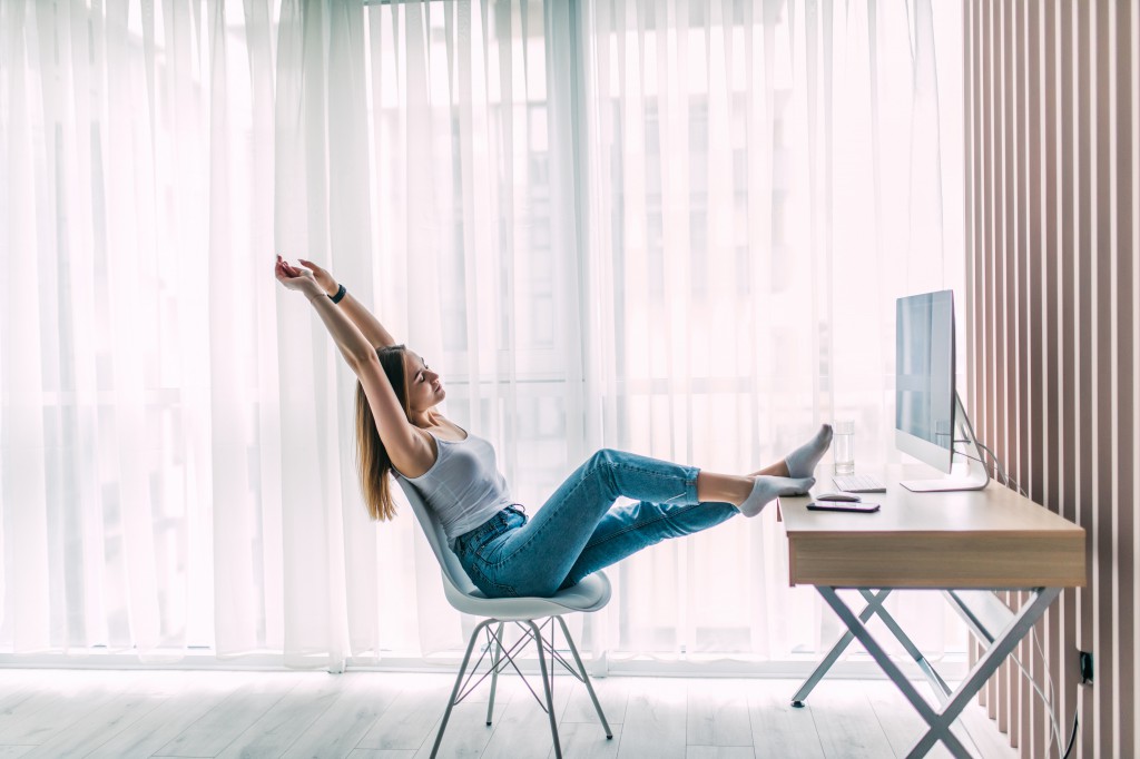 Young woman freelancer stretching and relaxing working on laptop in home office